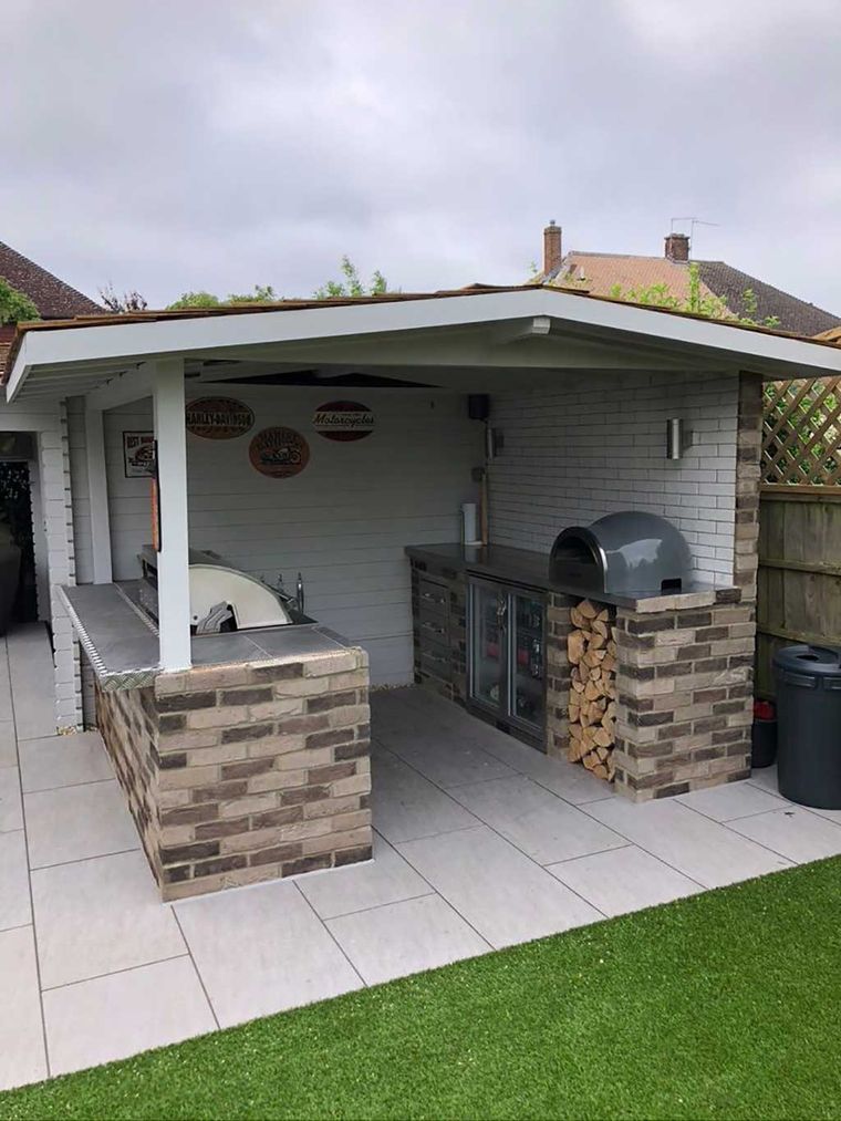 Covered outdoor kitchen with a brick bar, pizza oven and porcelain patio